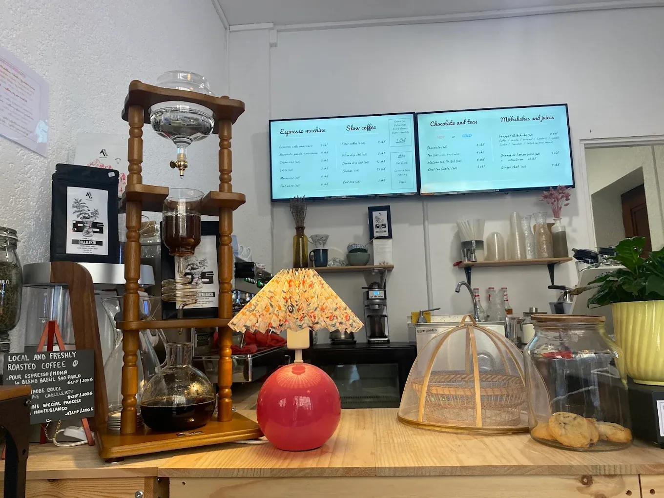Le comptoir d'Ogeessa Coffee à Genève : tour de cold drip en bois, lampe en coquillages colorée et pâtisseries sous cloche